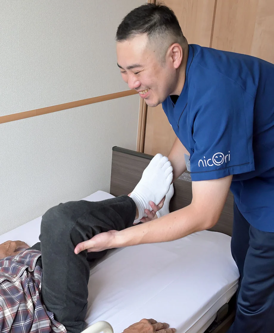 ベッドで施術を受ける利用者様を支えるスタッフ